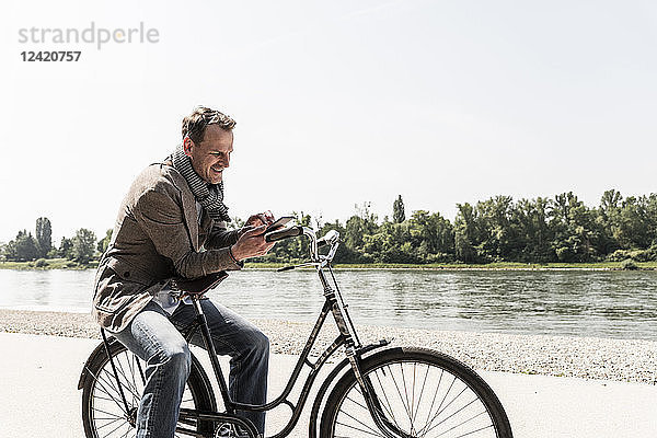 Mature man with bike using smartphone at Rhine riverbank