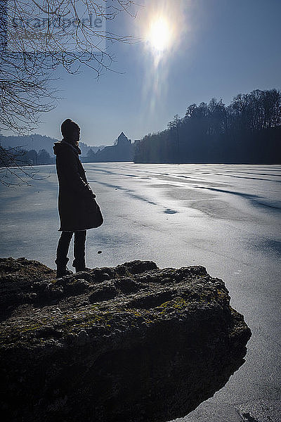 Woman standing on lakeshore in winter against the sun