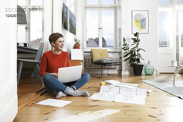 Woman sitting cross-legged on floor of her home  using laptop