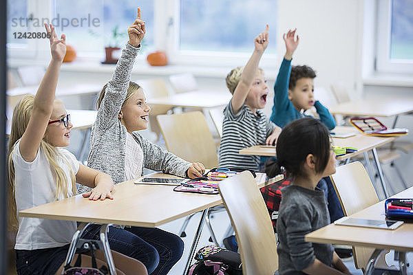 Happy pupils raising their hands in class