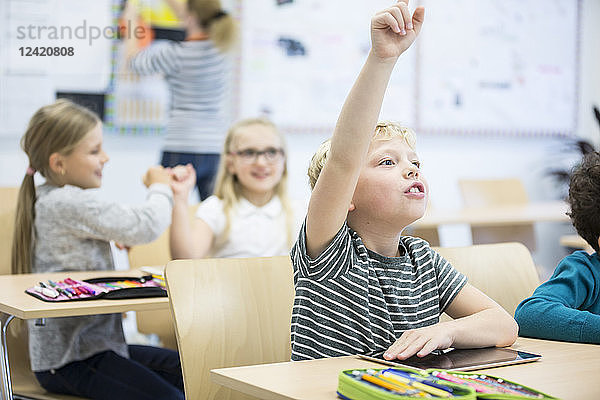 Schoolboy with tablet raising his hand in class