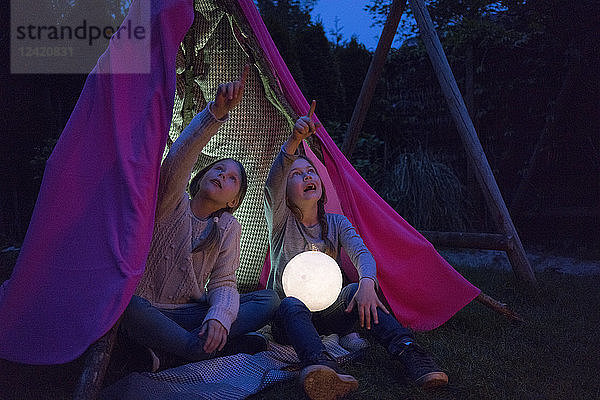 Two girls sitting in tipi  holding lamp as moon