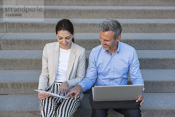 Two business people sitting side by side on stairs working together