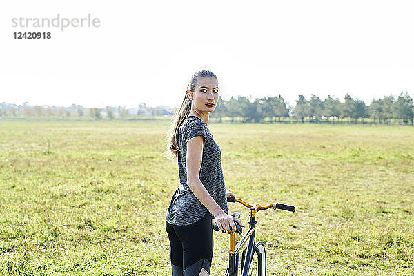 Sportive young woman with bicycle on a meadow