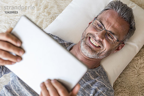 Mature man lying on pillow using a tablet