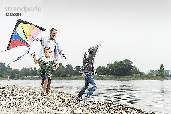 Happy father with two sons flying kite at the riverside