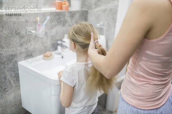 Mother combing daughter's hair in bathroom
