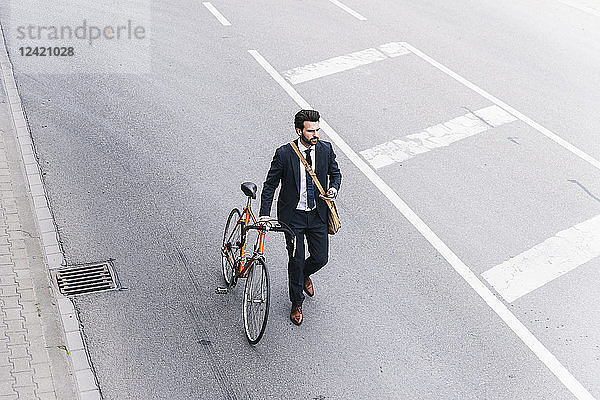 Businessman with bicycle and cell phone walking on the street