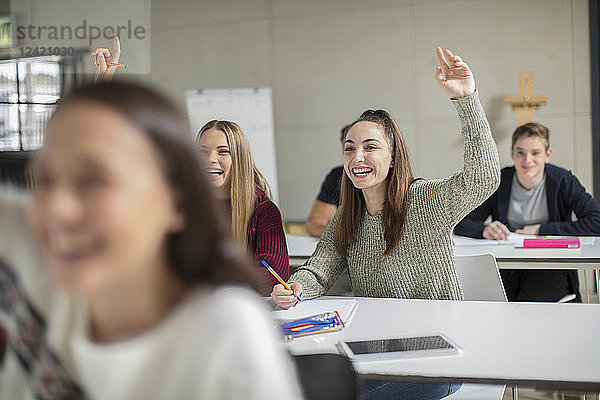 Happy teenage girls raising hands in class