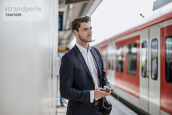 Businessman at the station with earbuds and cell phone