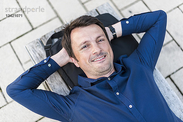 Portrait of smiling businessman lying on bench outdoors