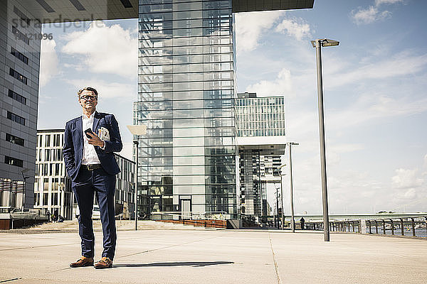 Mature businessman with cell phone standing outdoors