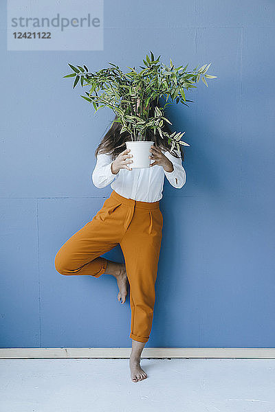 Pretty young woman holding potted plant in front of her face