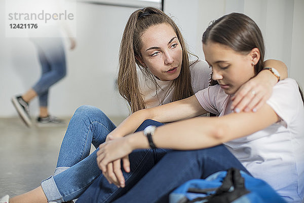Teenage girl consoling sad friend in school
