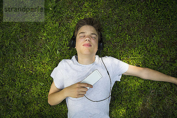 Portrait of boy lying on meadow listening music with headphones and smartphone