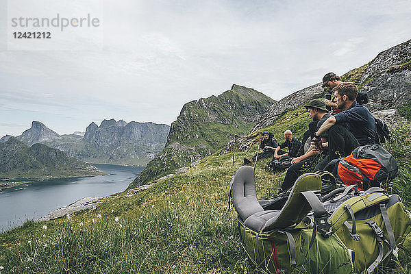 Norway  Lofoten  Moskenesoy  Group of young men sitting on grass  looking over Kjerkefjord