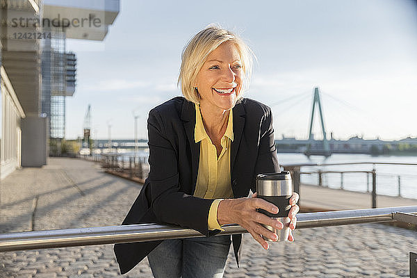 Happy senior businesswoman with takeaway coffee at the riverside