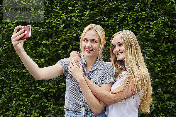 Two happy young women taking a selfie at a hedge