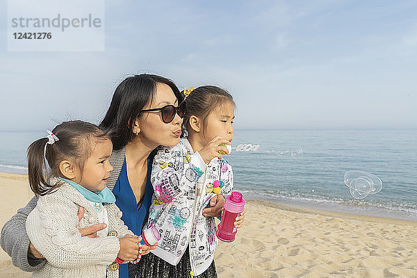 Mother with two daughters blowing soap bubbles on the beach