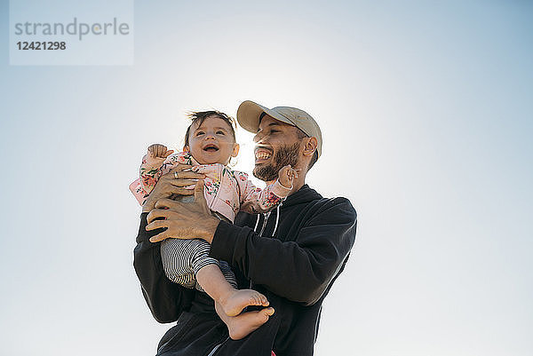 Laughing father holding baby girl at backlight