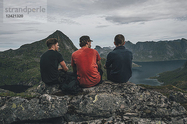 Norway  Lofoten  Moskenesoy  Three young men sitting on a rock  looking over Kjerkefjord
