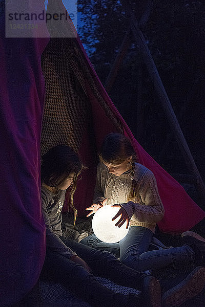 Two girls sitting in tipi  holding lamp as moon