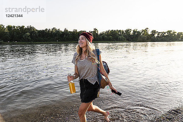 Young woman walking barefoot on riverside  earphones and smartphone