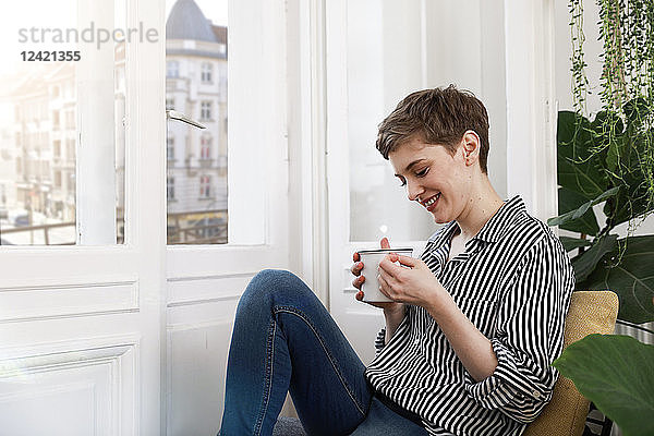 Happy woman sitting relaxed at window  drinking coffee