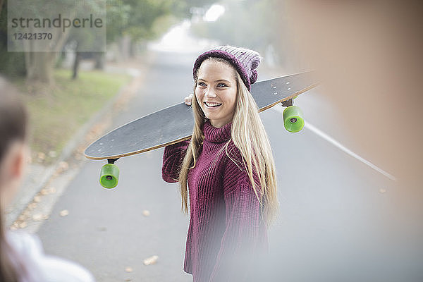 Smiling teenage girl holding skateboard meeting with friend