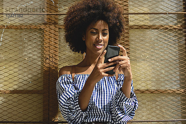 Portrait of fashionable young woman with curly hair looking at smartphone