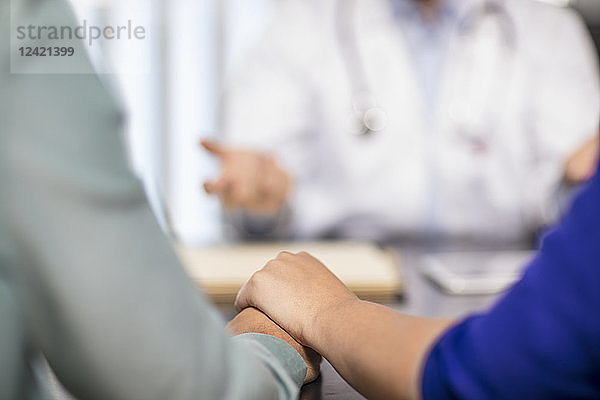 Doctor and couple holding hands in medical practice