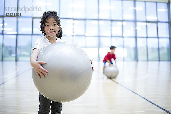 Portrait of smiling schoolgirl holding gym ball in gym class
