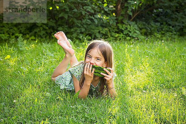 Portrait of little girl lying on a meadow eating watermelon