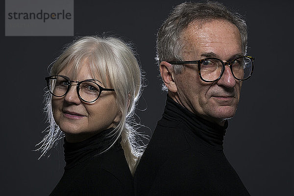 Portrait of senior couple wearing glasses in front of dark background