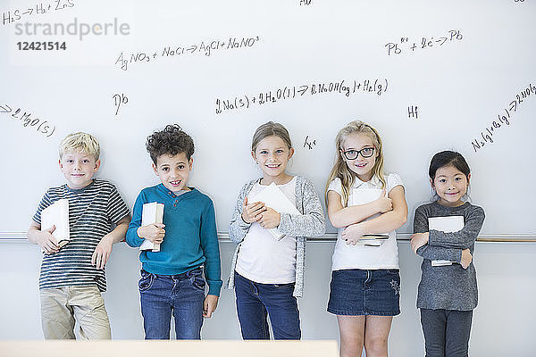 Portrait of smiling pupils standing at whiteboard with formulas in class