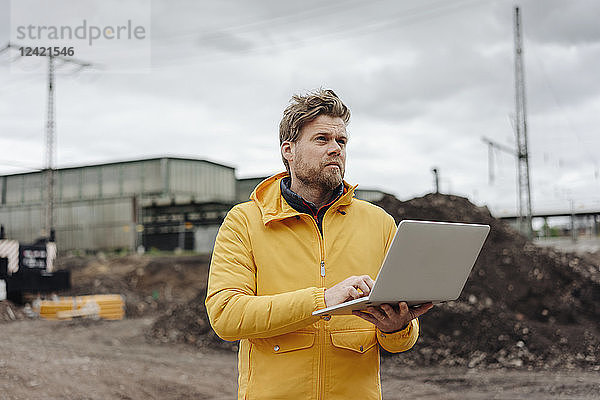 Man holding laptop  construction site in the background