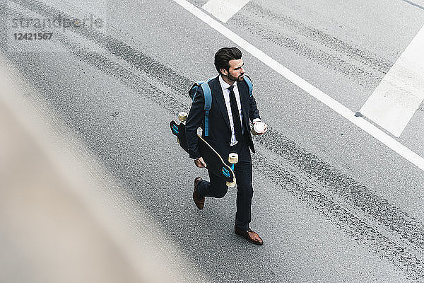 Businessman with takeaway coffee and skateboard walking on the street
