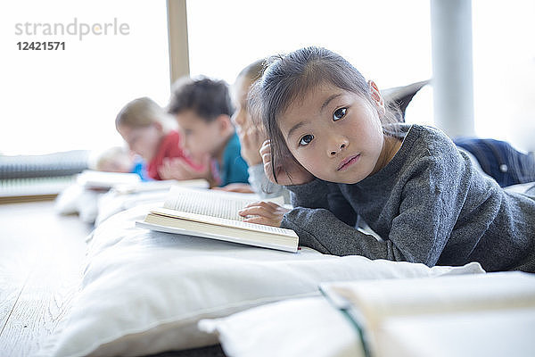 Portrait of schoolgirl lying on the floor with classmates reading book in school break room
