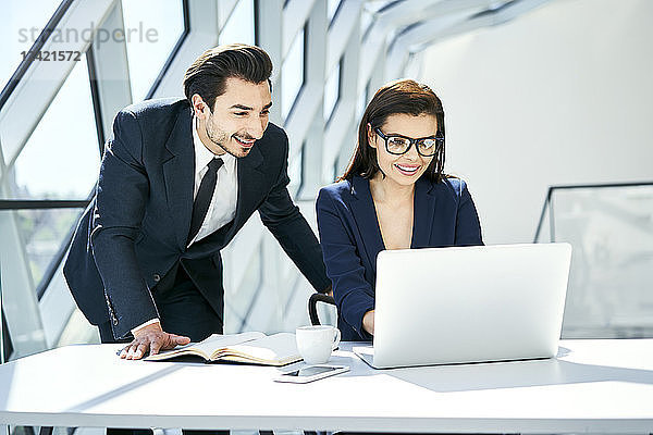 Smiling businesswoman and businessman using laptop at desk in modern office