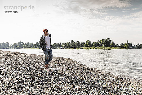Mature man with red beanie walking at Rhine riverbank