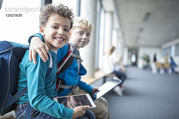 Portrait of two smiling schoolgboys with tablet embracing