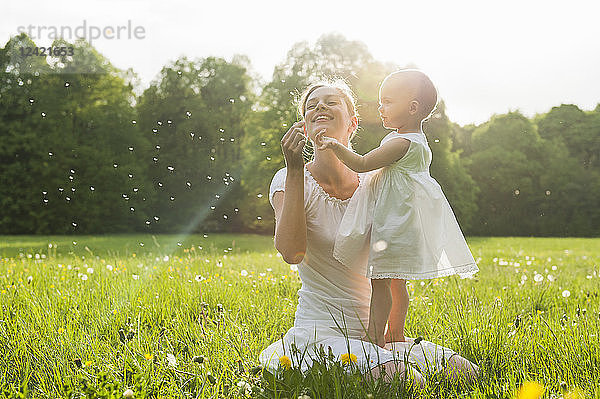 Mother and daughter with blowball on meadow in summer