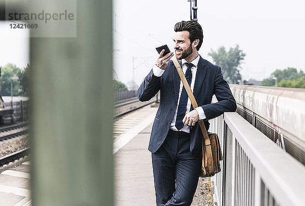Smiling businessman using cell phone at the platform