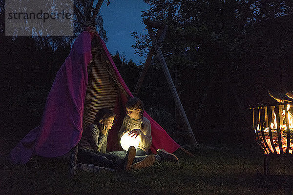 Two girls sitting in tipi  holding lamp as moon