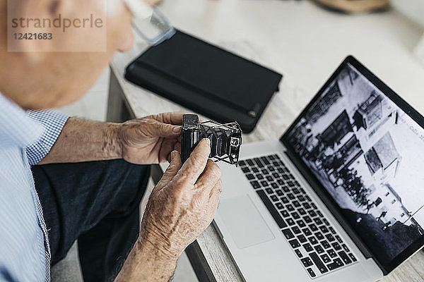 Senior man using laptop and holding his old photo camera  screen with old photo