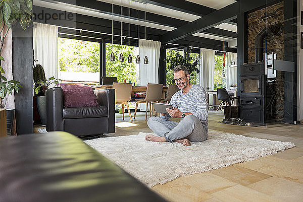 Smiling mature man sitting on carpet at home using a tablet
