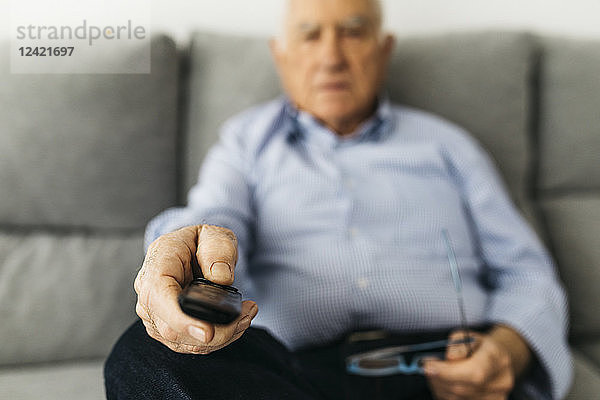 Senior man watching TV from the couch at home  focused on hand