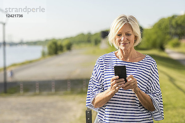 Smiling senior woman using cell phone at riverbank