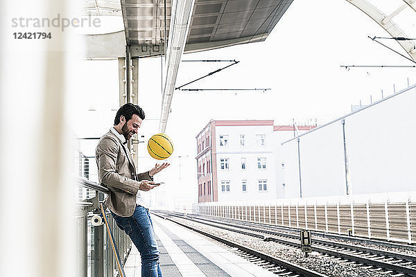 Smiling young man with cell phone and basketball at the station platform