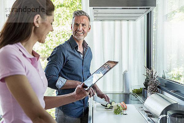 Happy couple in kitchen at home cooking and using a tablet